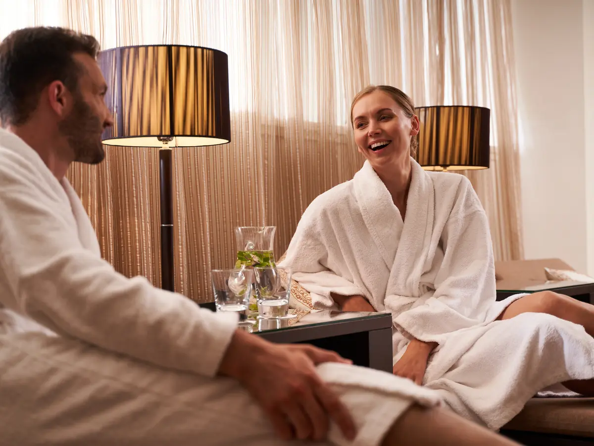 A couple in bathrobes laughs together in the relaxation room—relaxation and social connections as part of healthy aging A couple in bathrobes laughs together in the relaxation room—relaxation and social connections as part of healthy aging