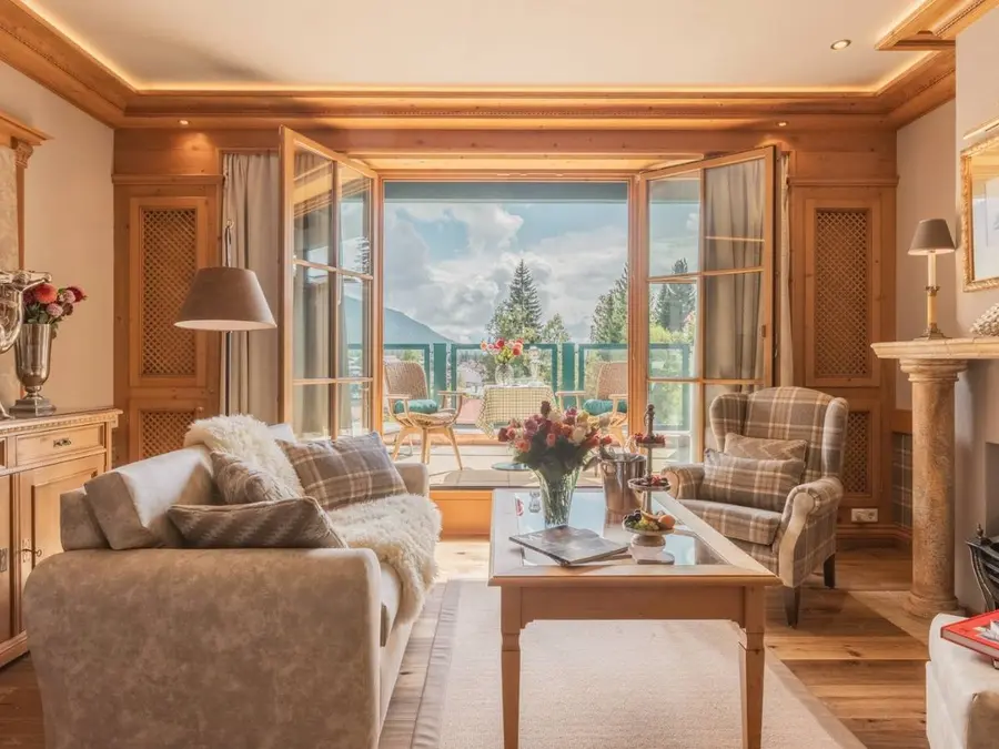 Living area of the Junior Suite at the Alpin Resort Sacher Seefeld, featuring wood paneling, a sofa, and a view of the balcony