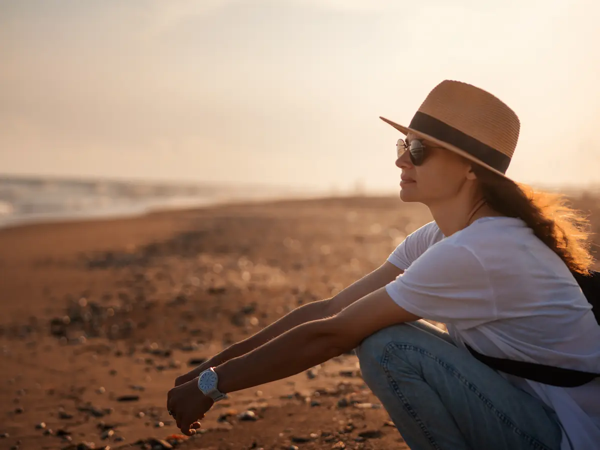 A woman wearing a hat enjoys a peaceful break on the beach at sunset—time to focus on her own health A woman wearing a hat enjoys a peaceful break on the beach at sunset—time to focus on her own health