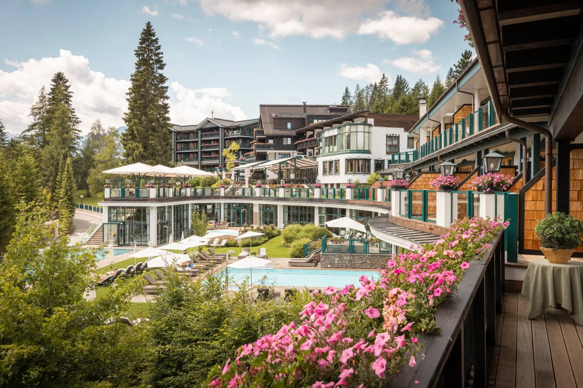 Alpin Resort Sacher Seefeld in the Summer: View from the flower-adorned balcony of the outdoor pool, sunbathing lawn, and hotel building