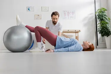 Frau trainiert unter physiotherapeutischer Anleitung mit Gymnastikball – gesund länger leben